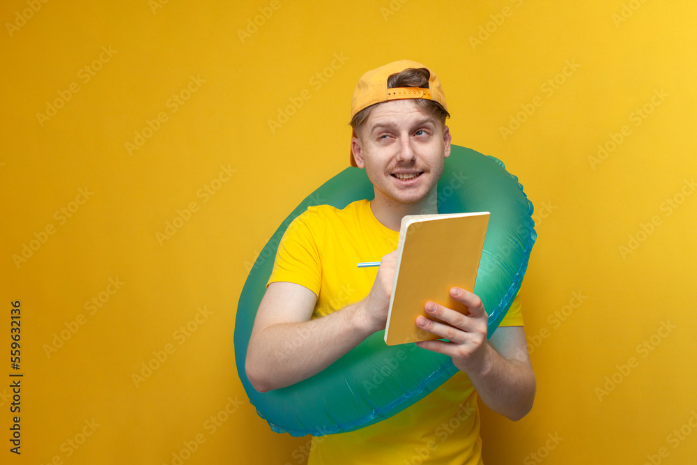young pensive guy in summer clothes and glasses on vacation with an inflatable circle writes in a notebook young pensive guy in summer clothes and glasses on vacation with an inflatable circle writes in a notebook