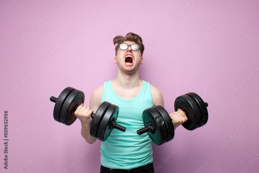 non-athletic guy in glasses holds heavy dumbbells on a pink background and trains, motivated nerd goes in for sports non-athletic guy in glasses holds heavy dumbbells on a pink background and trains, motivated nerd goes in for sports