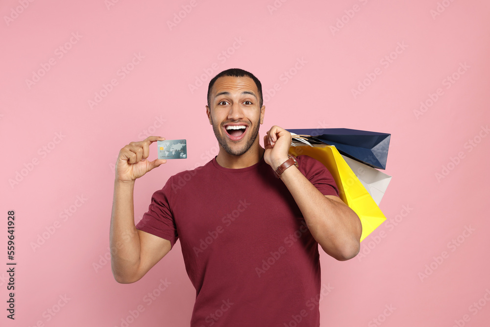 Happy African American man with shopping bags and credit card on pink background Happy African American man with shopping bags and credit card on pink background