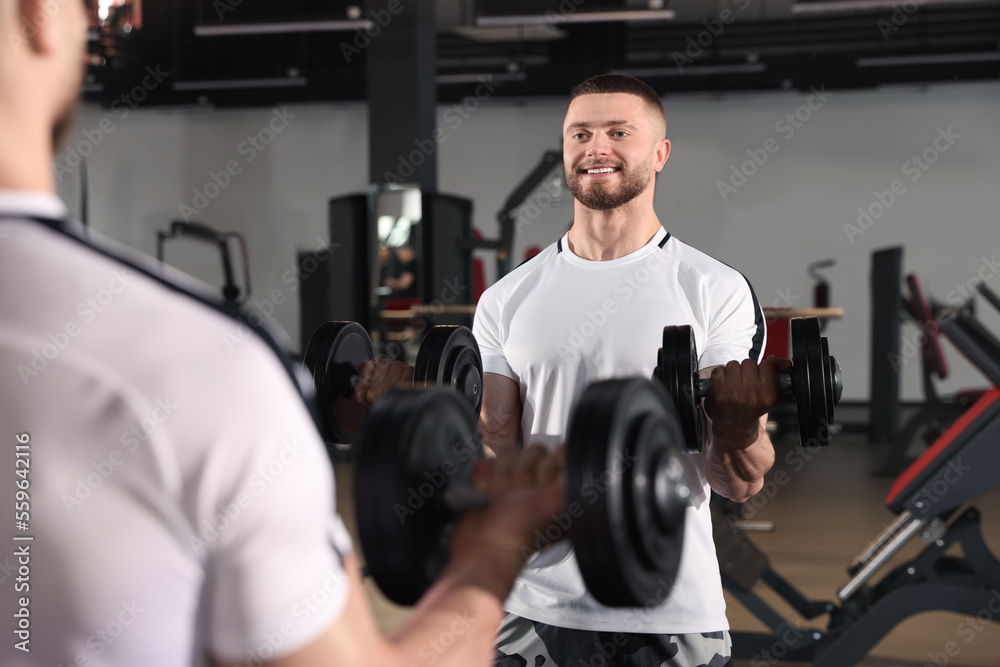 Man training with dumbbells near mirror in gym Man training with dumbbells near mirror in gym