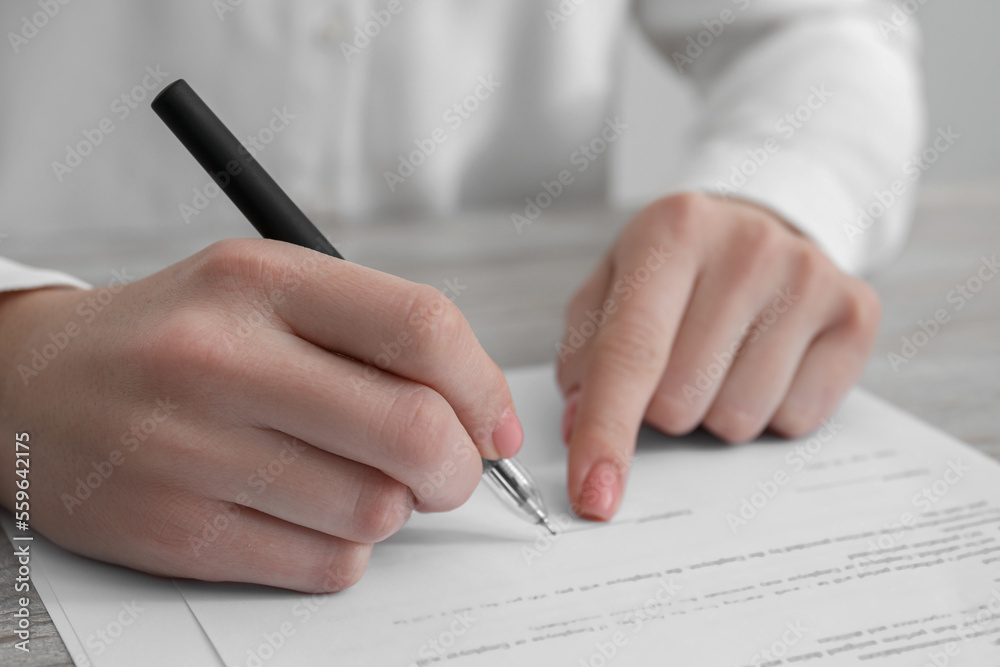 Woman signing documents at wooden table in office, closeup Woman signing documents at wooden table in office, closeup
