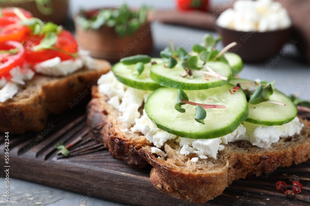Delicious sandwich with cucumber, microgreens and cheese on wooden board, closeup