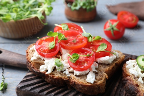 Delicious sandwich with cherry tomatoes, microgreens and cheese on wooden board, closeup