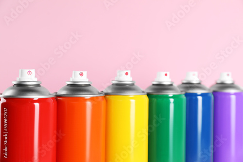 Colorful cans of spray paints on pink background, closeup