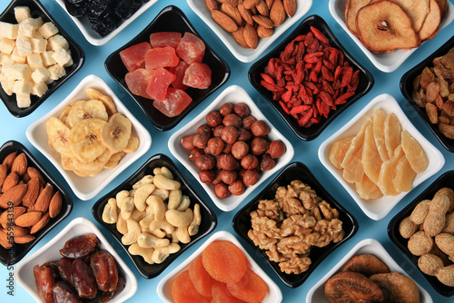 Bowls with dried fruits and nuts on light blue background, flat lay