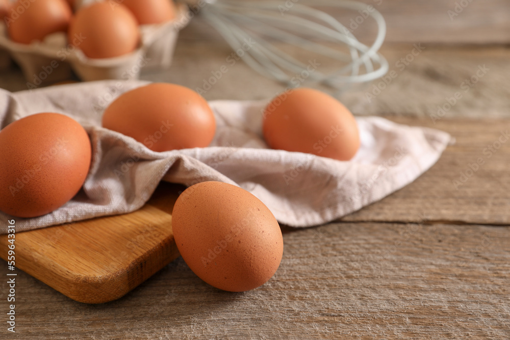 Raw chicken eggs, napkin, board and whisk on wooden table, closeup Raw chicken eggs, napkin, board and whisk on wooden table, closeup