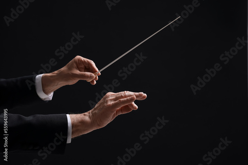 Professional conductor with baton on black background, closeup