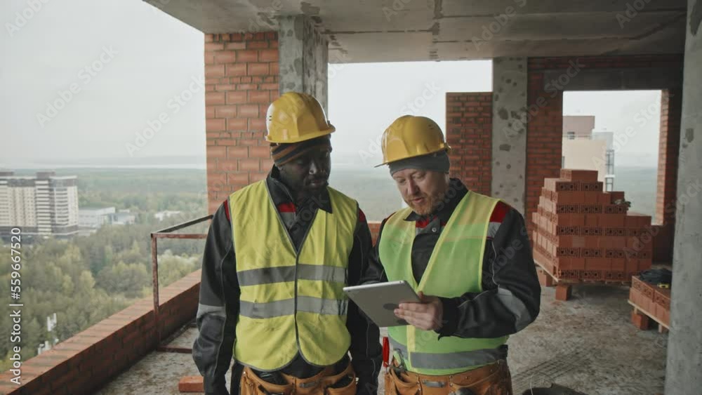 Ethnically diverse construction workers looking at blueprint on digital tablet screen and discussing plan Ethnically diverse construction workers looking at blueprint on digital tablet screen and discussing plan