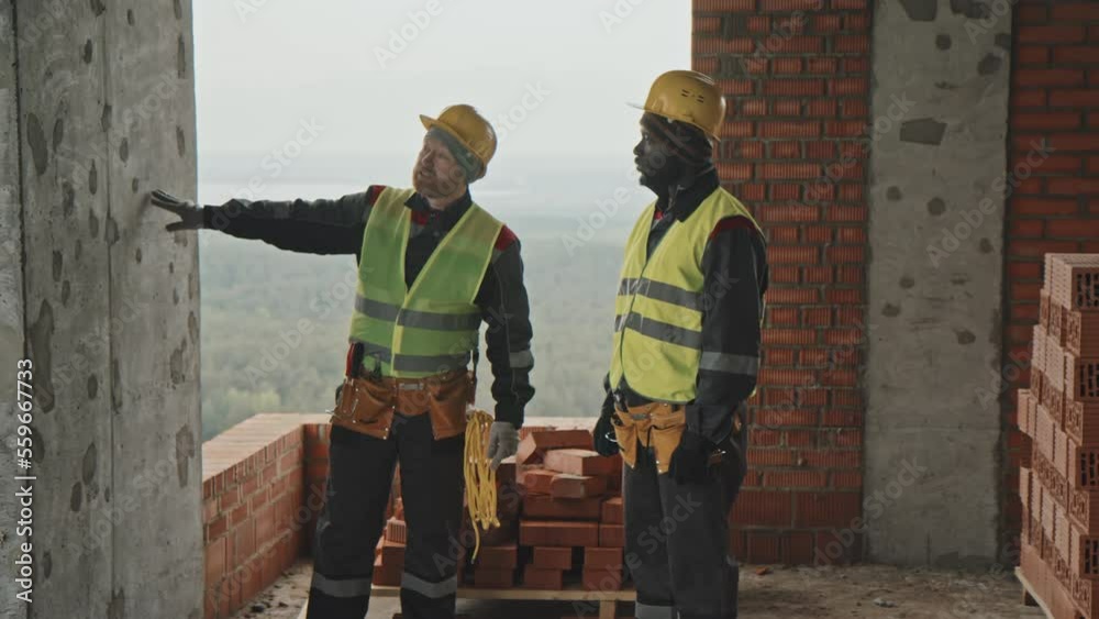 Medium long shot of two ethnically diverse construction workers planning work with bricks Medium long shot of two ethnically diverse construction workers planning work with bricks