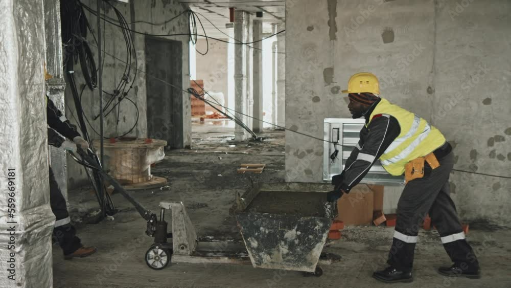 Side view of ethnically diverse construction workers carefully pulling and pushing cart full of mortar Side view of ethnically diverse construction workers carefully pulling and pushing cart full of mortar