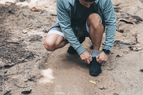 Sport man tying jogging shoes in the forest. Outdoor workout, Healthy lifestyle concept.