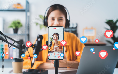 Vlogger live streaming podcast review on social media, Young Asian woman use microphones wear headphones with laptop record video. Content creator concept. photo