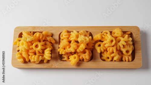 Cheetos is a crunchy corn puff snack. Bright orange cheese puffs in a wooden board.