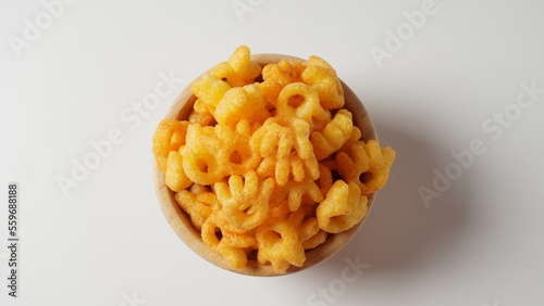 Cheetos is a crunchy corn puff snack. Bright orange cheese puffs in a wooden bowl.