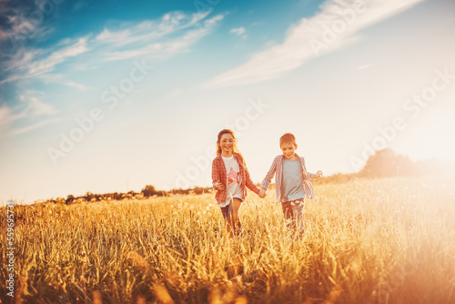 Two children running on the summer field by holding hands.