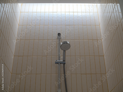 Stainless steel shower with bar mounted on vintage tiles wall, vertical pattern with yellow grout background in modern hotel bathroom.