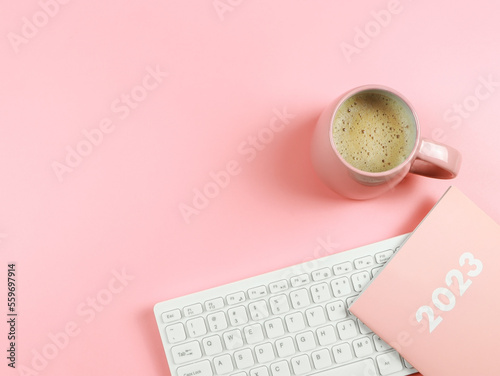 flat lay of computer keyboard, pink coffee cup  pink diary or planner  2023 on pink background with copy space.