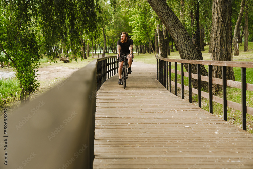 Adult handsome tattooed bearded man riding a bicycle in park