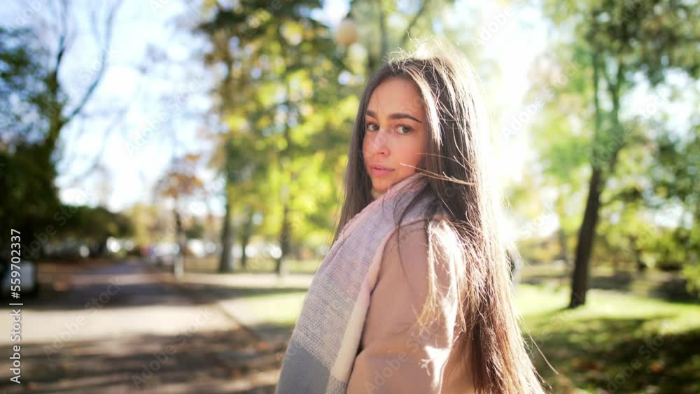 Portrait of happy girl walks forward on path of park and looks back looking at camera. Woman hold coffee in hands, smiling enjoying autumn nature outdoors landscape under sun rays. Leisure activity. Portrait of happy girl walks forward on path of park and looks back looking at camera. Woman hold coffee in hands, smiling enjoying autumn nature outdoors landscape under sun rays. Leisure activity.