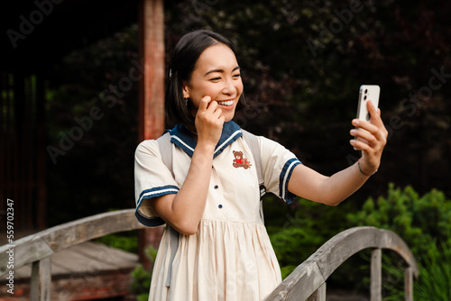 Young asian girl taking selfie on mobile phone while walking outdoors