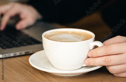 Close-up, a cup of coffee and on a blurred background with a laptop.