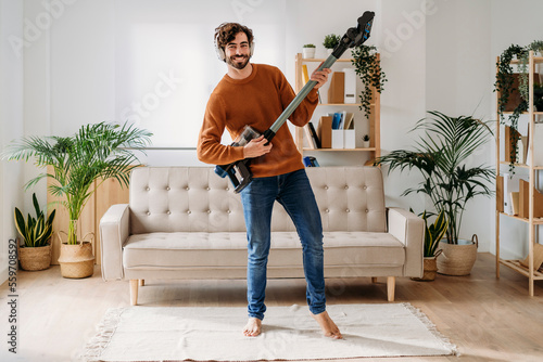 Happy man playing guitar on vacuum cleaner at home