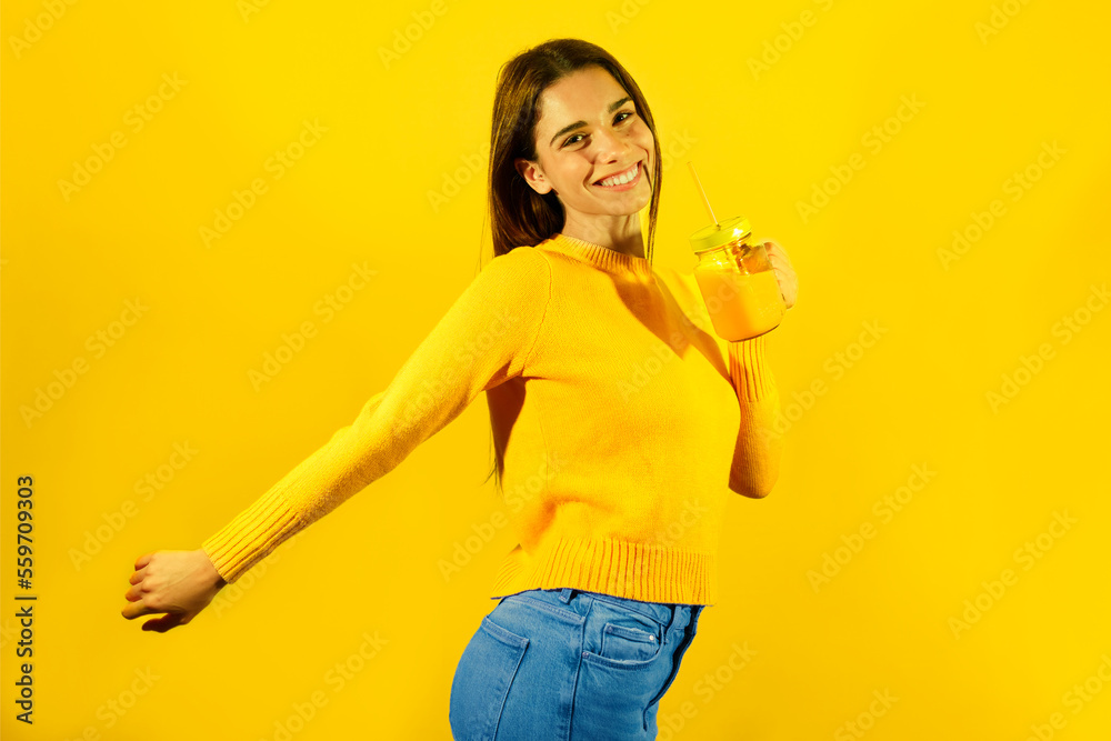 Happy young woman holding glass of orange juice against yellow background Happy young woman holding glass of orange juice against yellow background