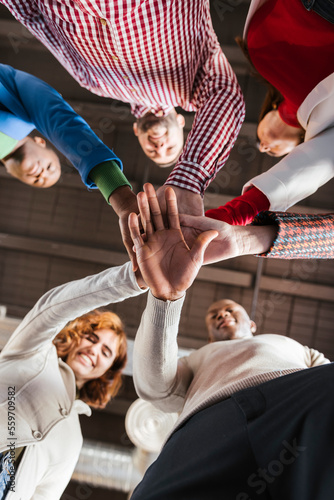 Happy multiracial businesswomen and businessmen stacking hands photo