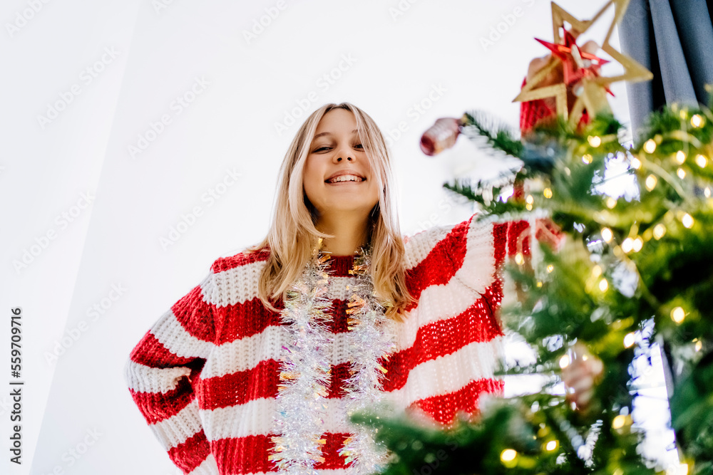 Happy girl wearing tinsel standing by Christmas tree at home Happy girl wearing tinsel standing by Christmas tree at home