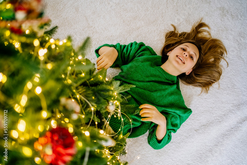 Happy girl lying on carpet under illuminated Christmas tree at home photo