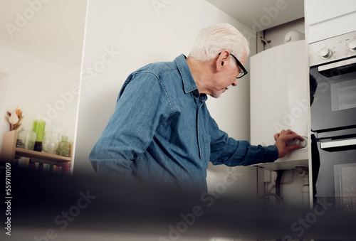 Senior man adjusting boiler for energy saving at home photo
