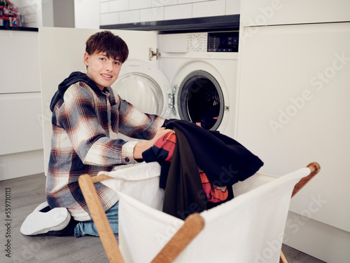 Smiling boy putting laundry into washing machine at home photo