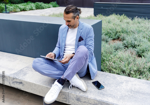 Mature man using tablet PC sitting on bench photo