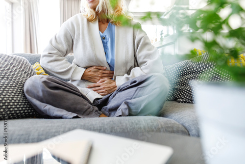 Woman having stomach ache sitting on sofa at home photo
