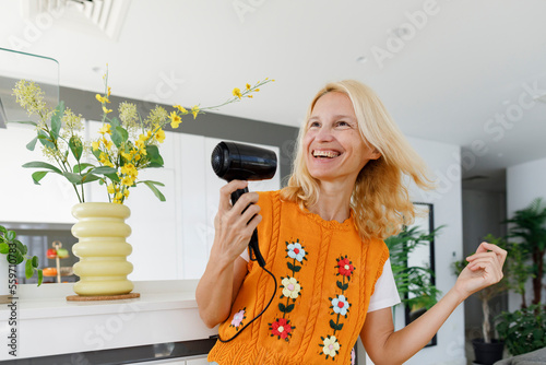 Cheerful woman dancing with hairdryer at home photo