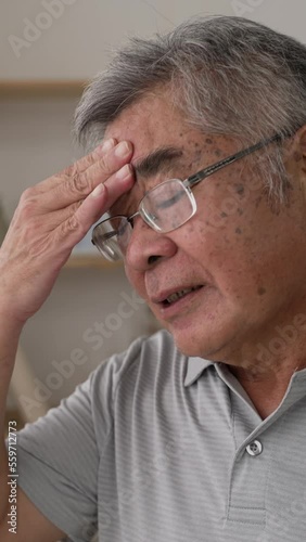 Vertical Screen: elderly man standing in living room look in window distance thinking. thoughtful male rest at home feel sad considering future. worried old male hand touch forehead