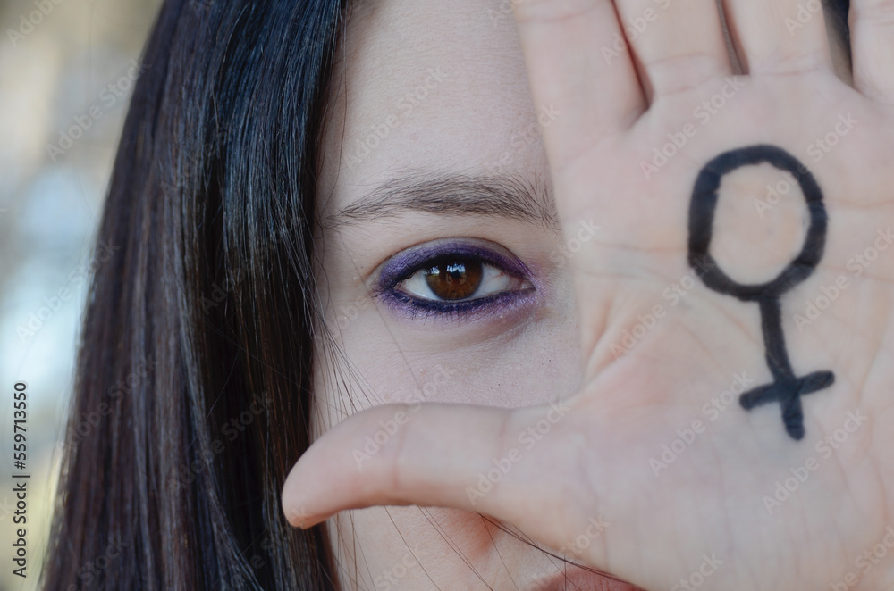Hand of a woman with the feminist symbol. Main focus on the woman's eye ...