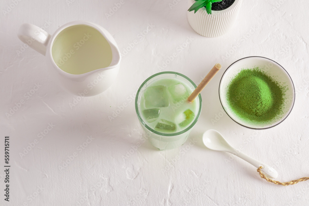 green healthy matcha latte tea with ice cubs on a white table with a bowl of matcha powder and milk jug with milk. top view. amino acids.