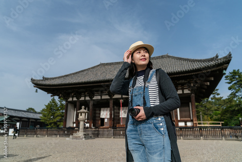 cheerful asian Japanese woman tourist keeping hand on her hat and looking up into sky to enjoy good weather while visiting kofuku-ji temple in nara japan © PR Image Factory