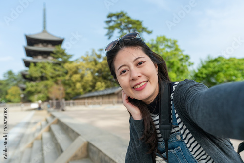 self portrait of smiling asian Japanese female visitor looking at camera with gojunoto pagoda of kofuku-ji temple at background in nara japan on a sunny day in spring