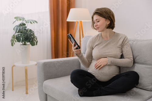 Obraz na plátně Happy pregnant millennial woman using smartphone at home, browsing pregnancy app