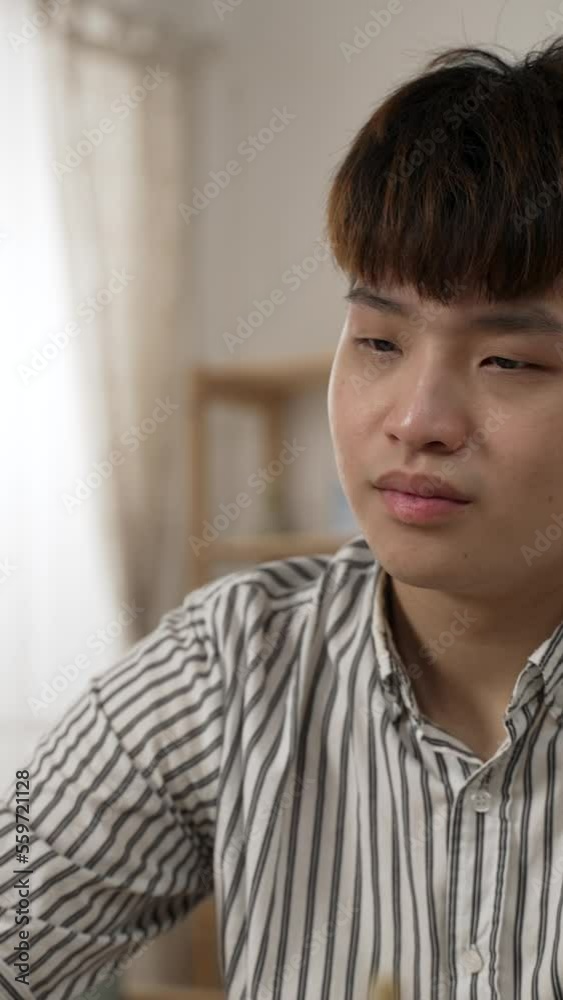 Vertical Screen: shoulder shot of a Korean male with poor eyesight is rubbing his tired eyes and blinking at the computer screen while working from home in the living room. Vertical Screen: shoulder shot of a Korean male with poor eyesight is rubbing his tired eyes and blinking at the computer screen while working from home in the living room.