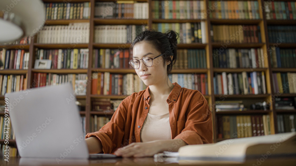 Concentrated female librarian working with books register on computer, keeping catalog