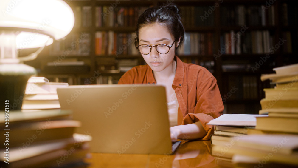 Asian female freelancer working late at night at city library, doing research Asian female freelancer working late at night at city library, doing research