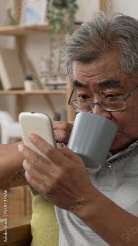 Vertical video: Elderly man reading online news on mobile phone and drinking coffee. old grey hair grandpa using cellphone and enjoy cup of morning tea.