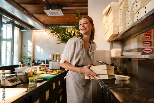 Young woman holding food boxes while working in restaurant kitchen photo