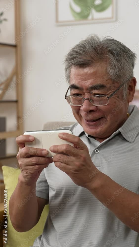 Vertical Screen: old man using mobile phone during quarantine time stay at home alone. happy older male looking at smartphone screen while play online game celebrating victory with yes gesture Vertical Screen: old man using mobile phone during quarantine time stay at home alone. happy older male looking at smartphone screen while play online game celebrating victory with yes gesture
