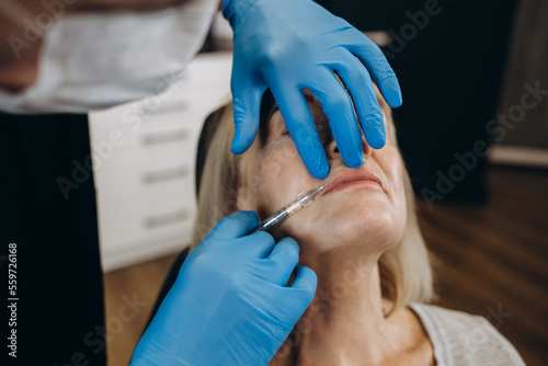 Botox  injection and antiaging with a senior woman in studio on a gray background with hands in gloves for treatment. Wrinkles  wellness and cosmetics with a mature female patient and plastic surgeon