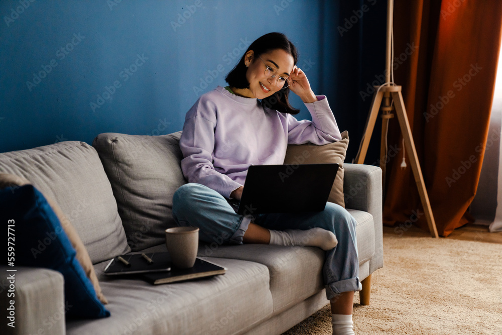 Smiling asian woman working on laptop while sitting on couch