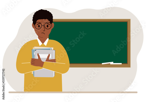 Male teacher with books on the background of the school board.